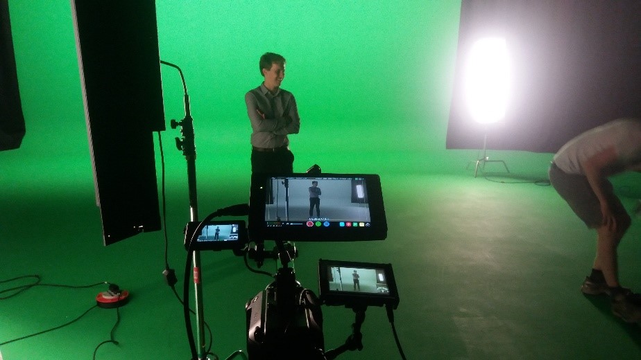 Matt stands in front of a green screen with a camera pointing at him in the foreground