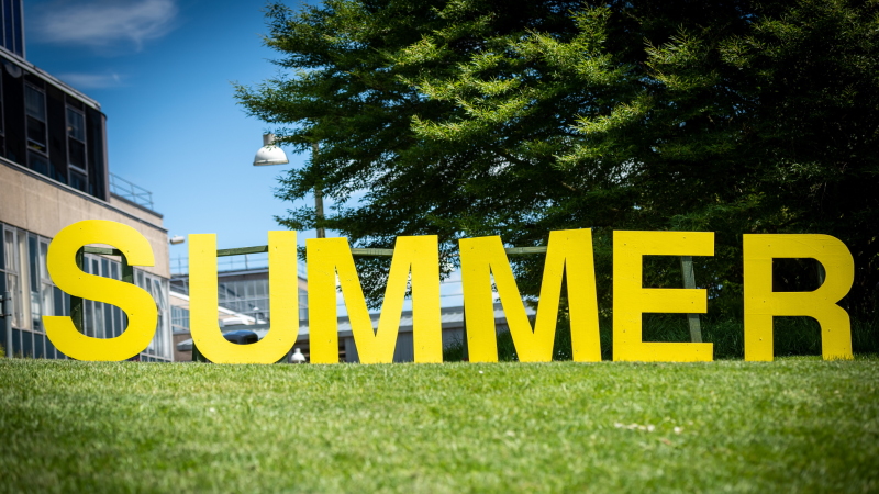 Large yellow capital letters spelling the word 'summer' located on campus by the lake as part of the Summer at Bath programme.