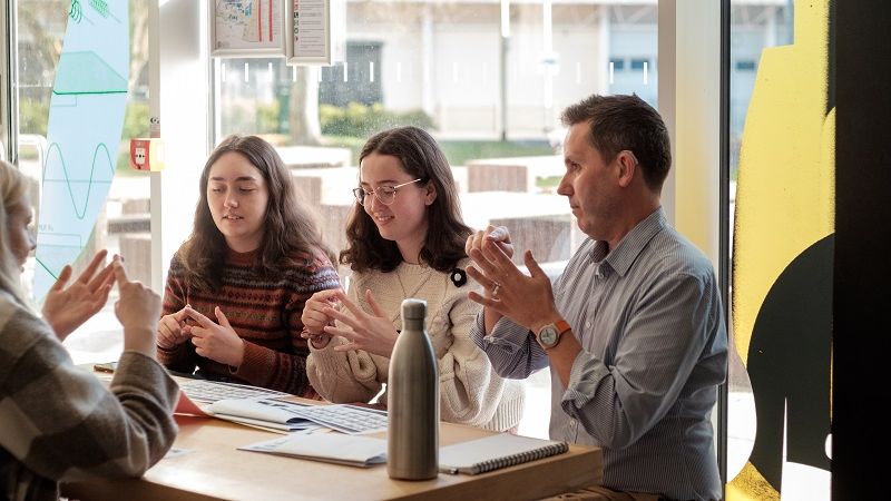 A member of staff and a group of students practising BSL at the Language Cafe on campus.