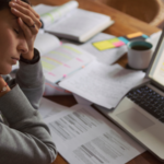 Woman sits at desk with laptop, looking tired