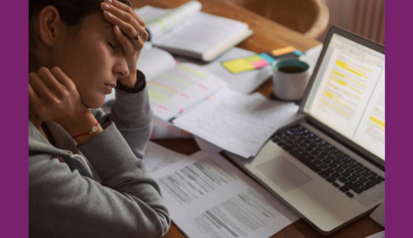 Woman sits at desk with laptop, looking tired