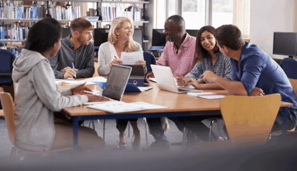 A group of students sitting at a table with laptops working together
