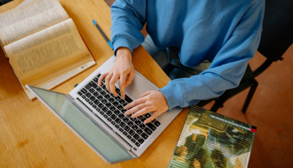 A photo of someone typing on a laptop with textbooks on either side