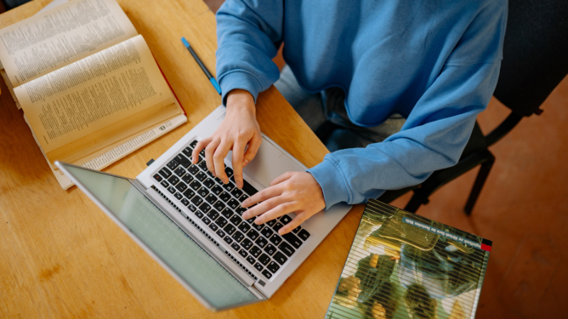 A photo of someone typing on a laptop with textbooks on either side