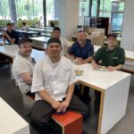 A group of Camps Services staff sat around a table in lime tree, smiling at the camera.