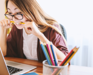 Lady biting pencil staring at computer screen