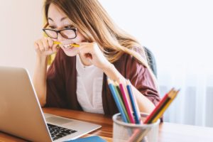 young woman looking worried at her laptop with a pencil in her mouth