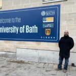 A photograph of Jhonatan in front of the University of Bath welcome sign