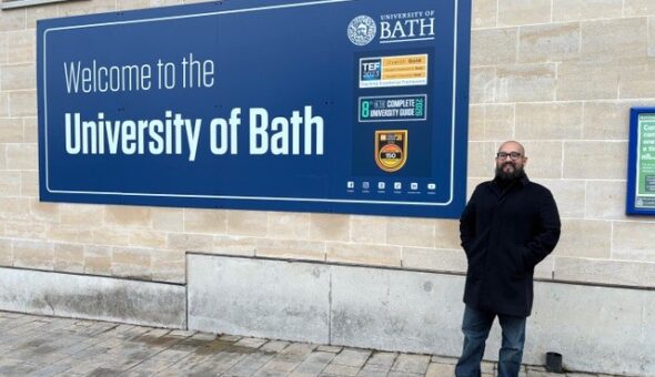 A photograph of Jhonatan in front of the University of Bath welcome sign