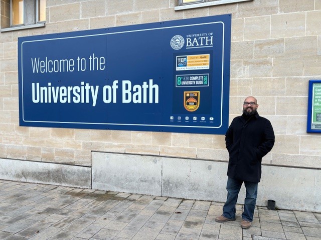 A photograph of Jhonatan in front of the University of Bath welcome sign