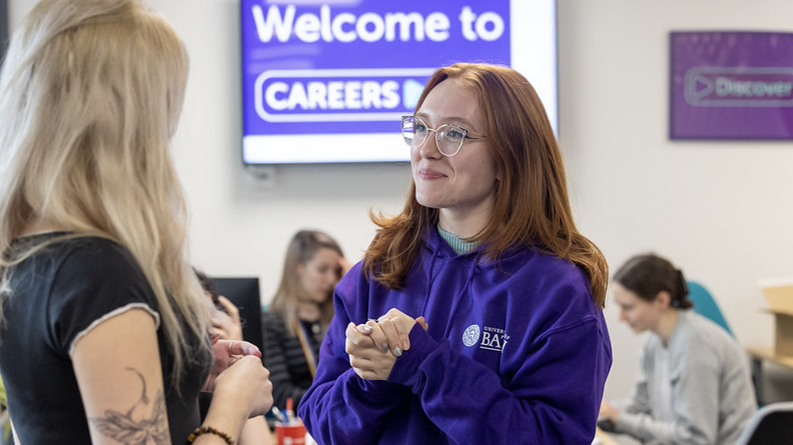 A photograph of Maddie talking to a student in the Careers Centre