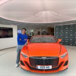 A photograph of Shyan Shah standing next to an orange Bentley