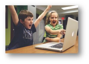 Two excited children looking at and pointing to a laptop screen