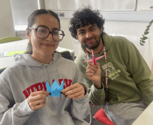 Photo of Nadia and Vivek smiling in an office holding origami cranes