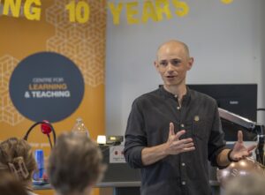 Male colleague speaking at front on room in front of banner