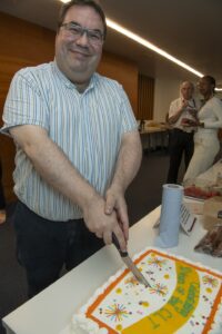 Male Colleague cutting 10 year celebratory cake