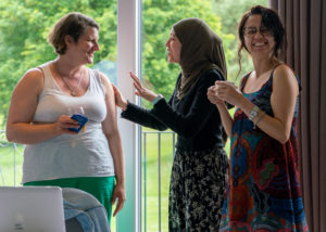 Three students chat during a break, one holds a teacup and smiles at the camera.