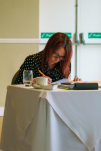 An academic sits writing at the desk with a pen.