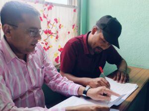 One person writing and another person pointing at the written information on a page