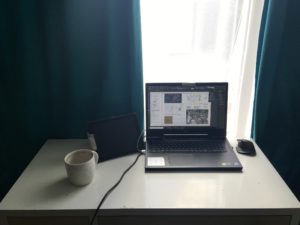 A desk with a laptop and a mug facing the window.