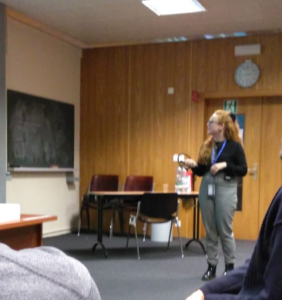 A lady with red haired glasses presenting in a meeting room.