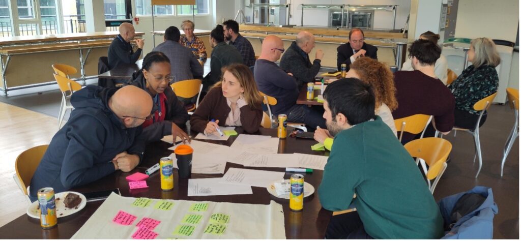people sit around tables in group discussions, using paper and sticky notes.