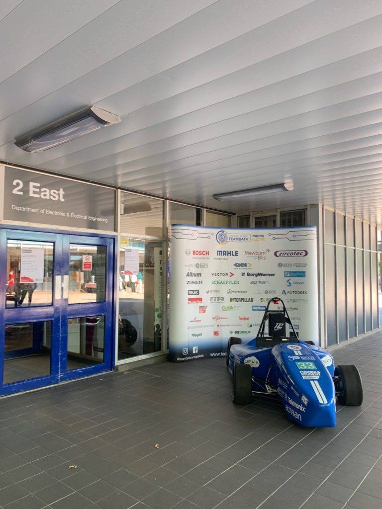 A photo of a race car and banner outside the entrance of the 2 East building on campus