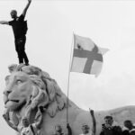 image of protestor standing on statue of lion with England flags