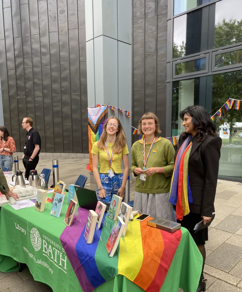 Two representatives from the Library with VP Rajani Naidoo operting the Library Stall, which is draped with a Pride flag and display books