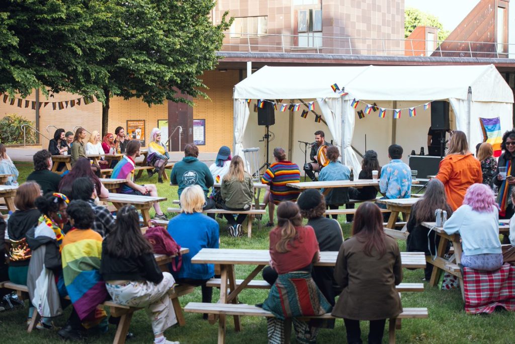 The crowd at Campus Pride watching a performance by Mother, who is sat beneath the marquee