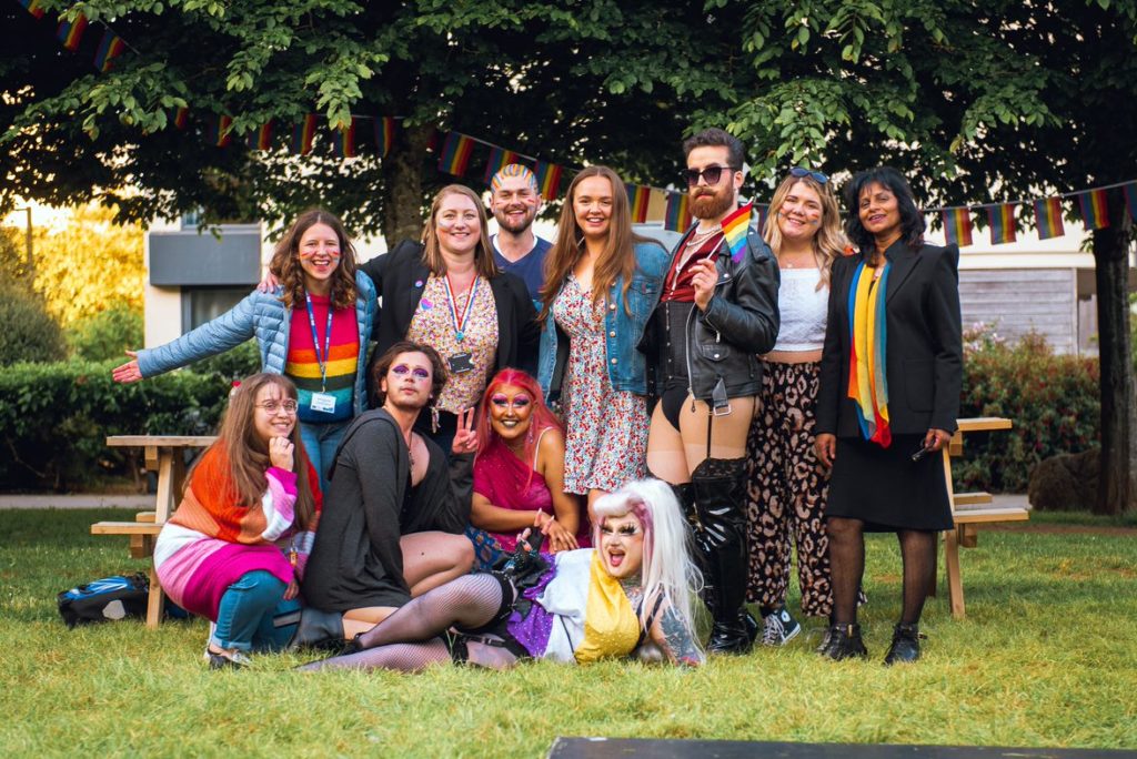 Drag performers, University of Bath staff and SU reps standing in line for a group photo. Four of them are crouched in front