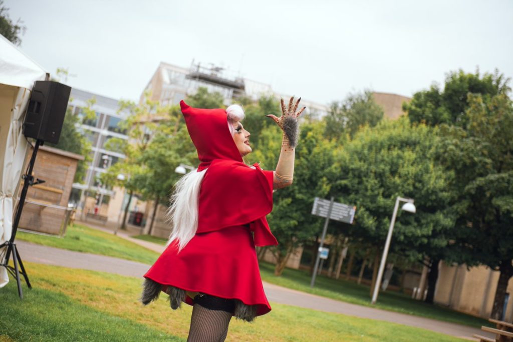 Drag artist, Remy Melee, dressed in a hooded red coat while performing one of their sets