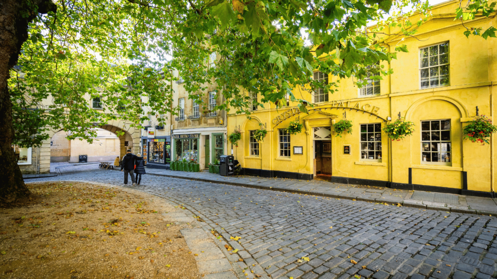 A bright yellow pub with a cobblestone path and a tree in front of it