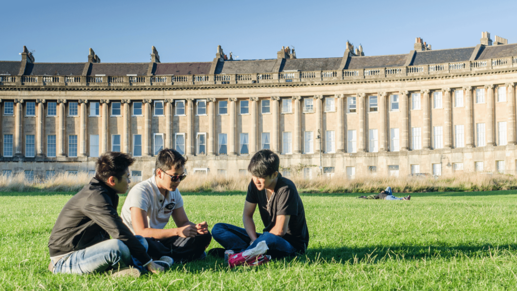 Three male students sat in the grass in front of the Royal Cresent