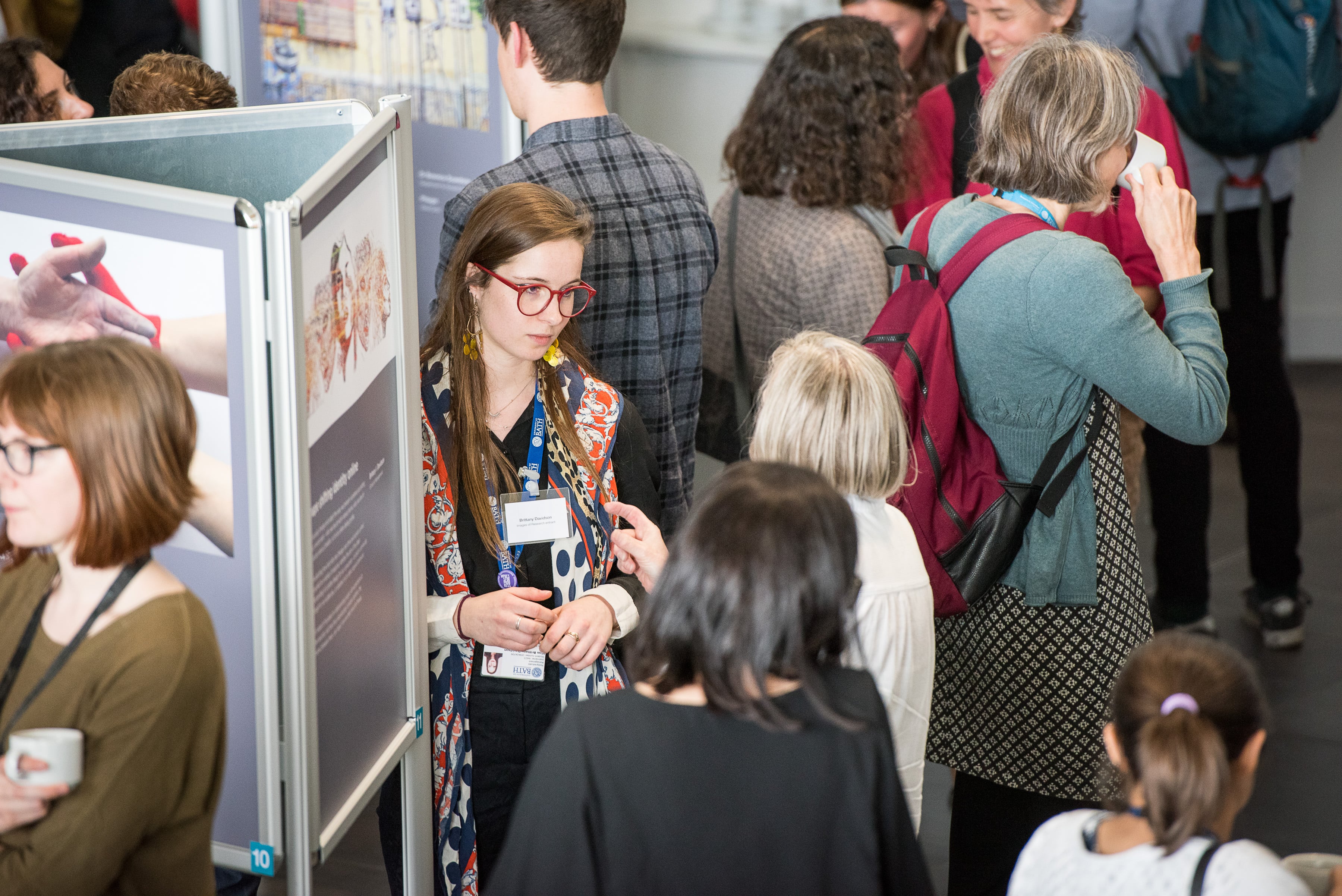 A female researcher next to an exhibition stand with their poster in conversation with a woman. 