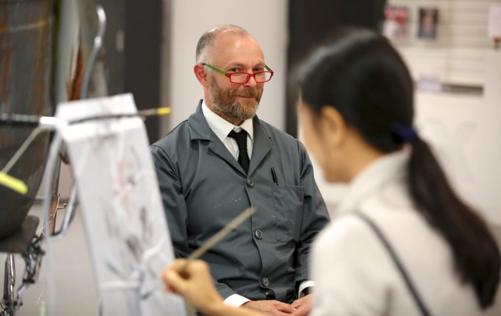 A man sits on a chair and is being drawn by an artist