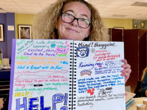 A white female holding a notebook open to two pages full of illustrations and diagrams