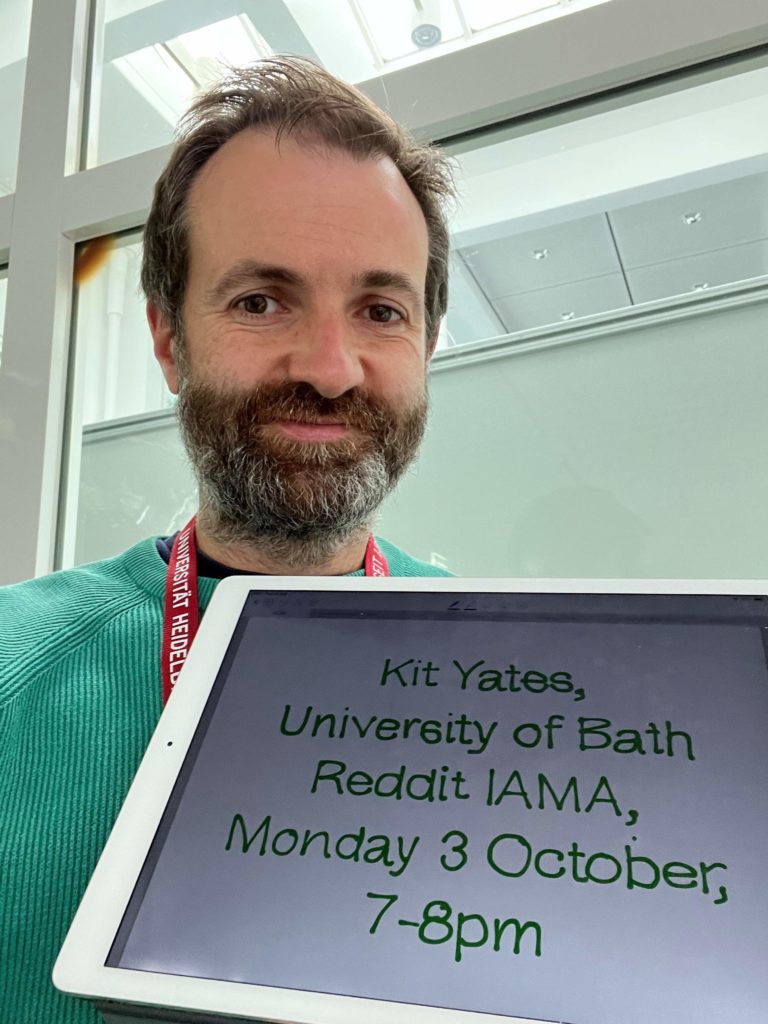 A man with a beard holding a tablet with the time and date of a Reddit AMA written on it.