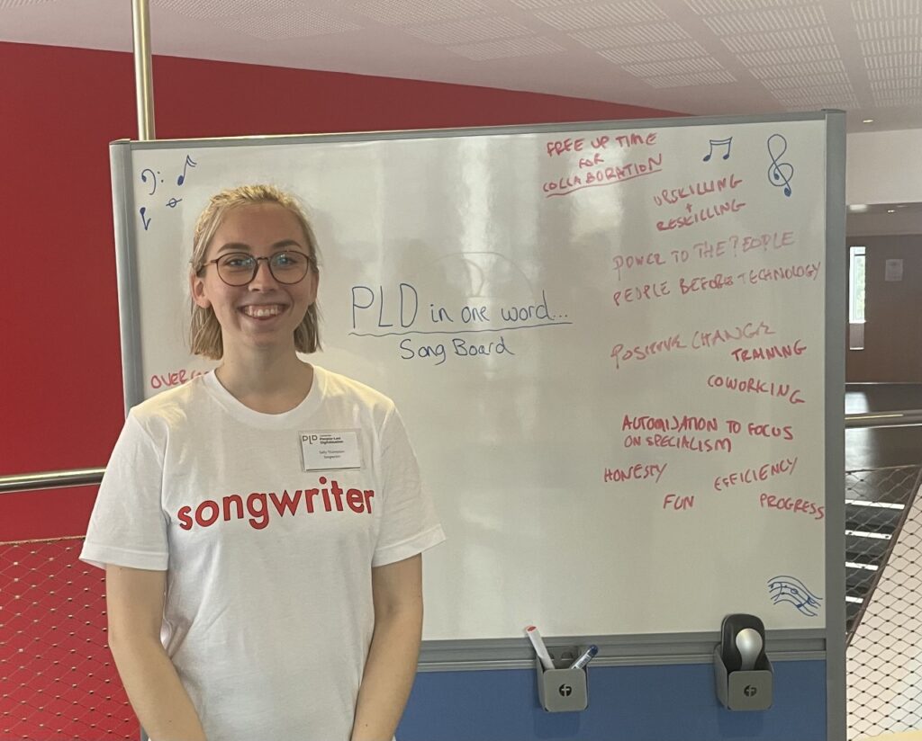 A white woman wearing a t-shirt with songwriter written on it standing in front of a whiteboard with song lyrics written on it.