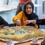 Community members gather sit around a table with a model of green spaces