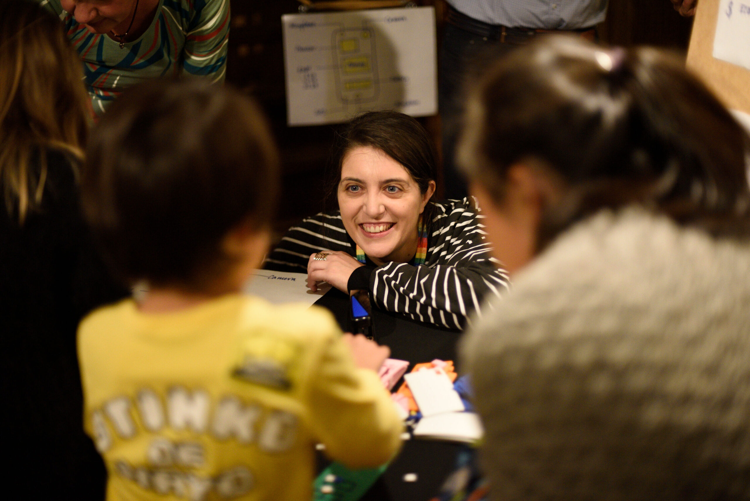 A research smiles up at an adult and young person who are curiously exploring whats on the table in front of them