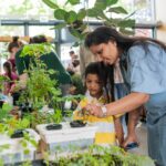 An adult and young person lean over a table full of plants