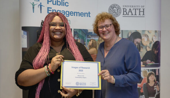 A woman with long pink hair holding a certificate with a woman in a blue top. Both are smiling at the camera.
