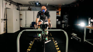 A man riding an indoor bike in a lab setting where his performance is being assessed using a range of physiological sensors including oxygen, muscle activation and motion. 