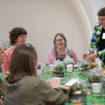 People talking around a table that has many small plants in glass domes on it.