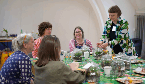 People talking around a table that has many small plants in glass domes on it.