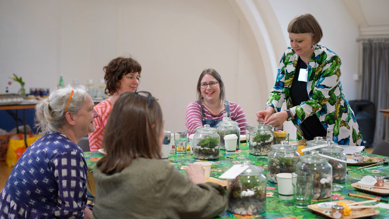 People talking around a table that has many small plants in glass domes on it.