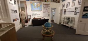 A large bright room with white walls containing many glass cabinets, tables and art on the walls, including a world map documented different places Haile Selassie visited