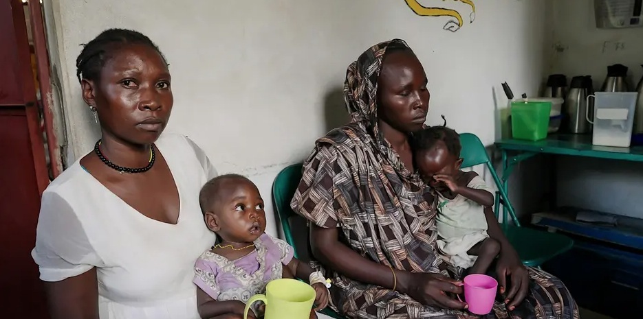 Two Sudanese women care for children sitting in their laps.