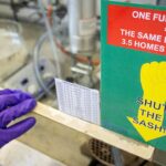 Gloved hand closes a fume cupboard with a sustainability sign on it